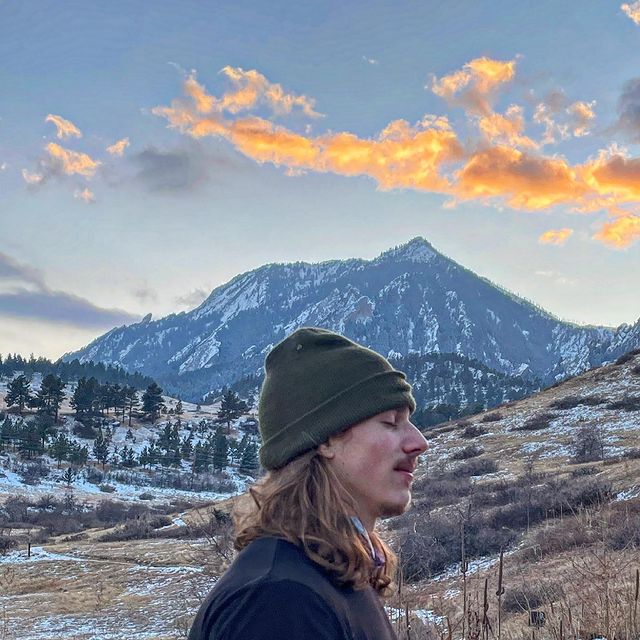 Christian in a beanie looking out at a snowy mountain at sunset