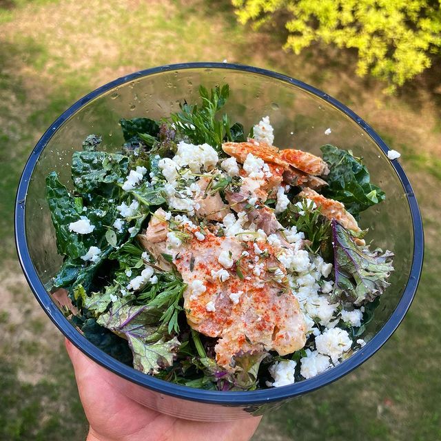 A bowl of greens topped with salmon and feta, held up over the grass
