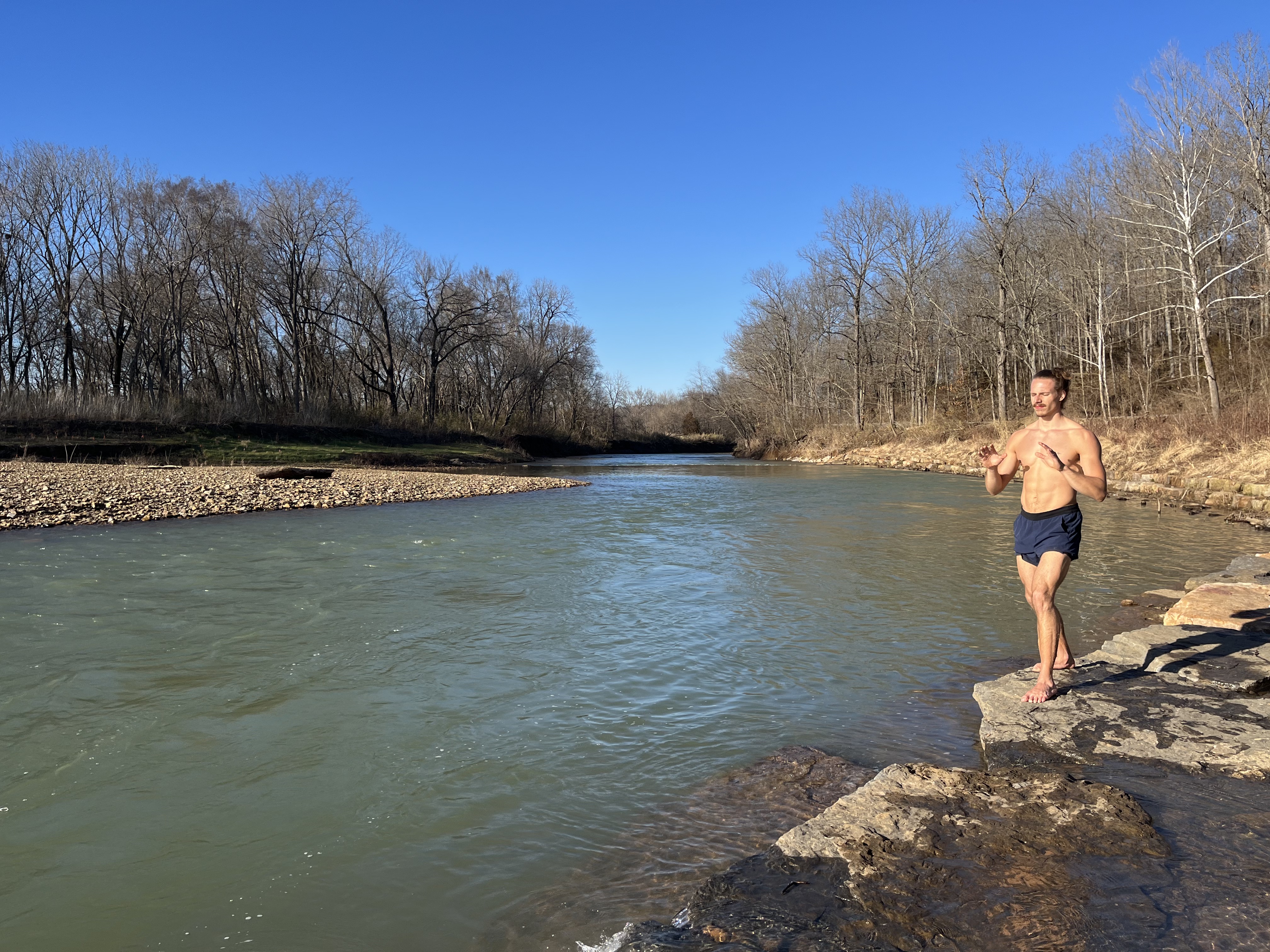Christian walking barefoot along a rocky riverbank on a clear winter day